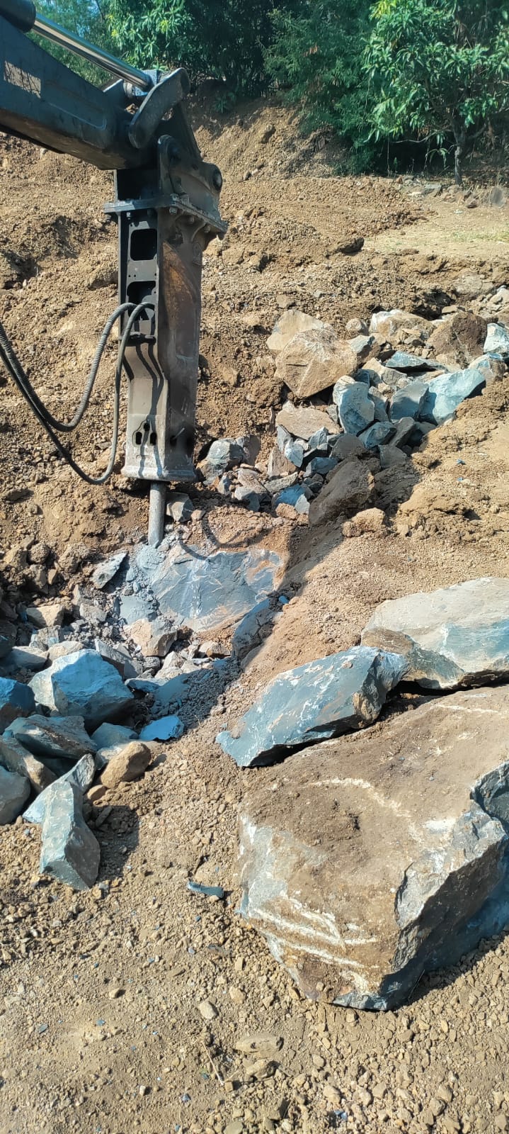 Hydraulic breaker attachment fracturing hard black basalt rock in the excavation pit