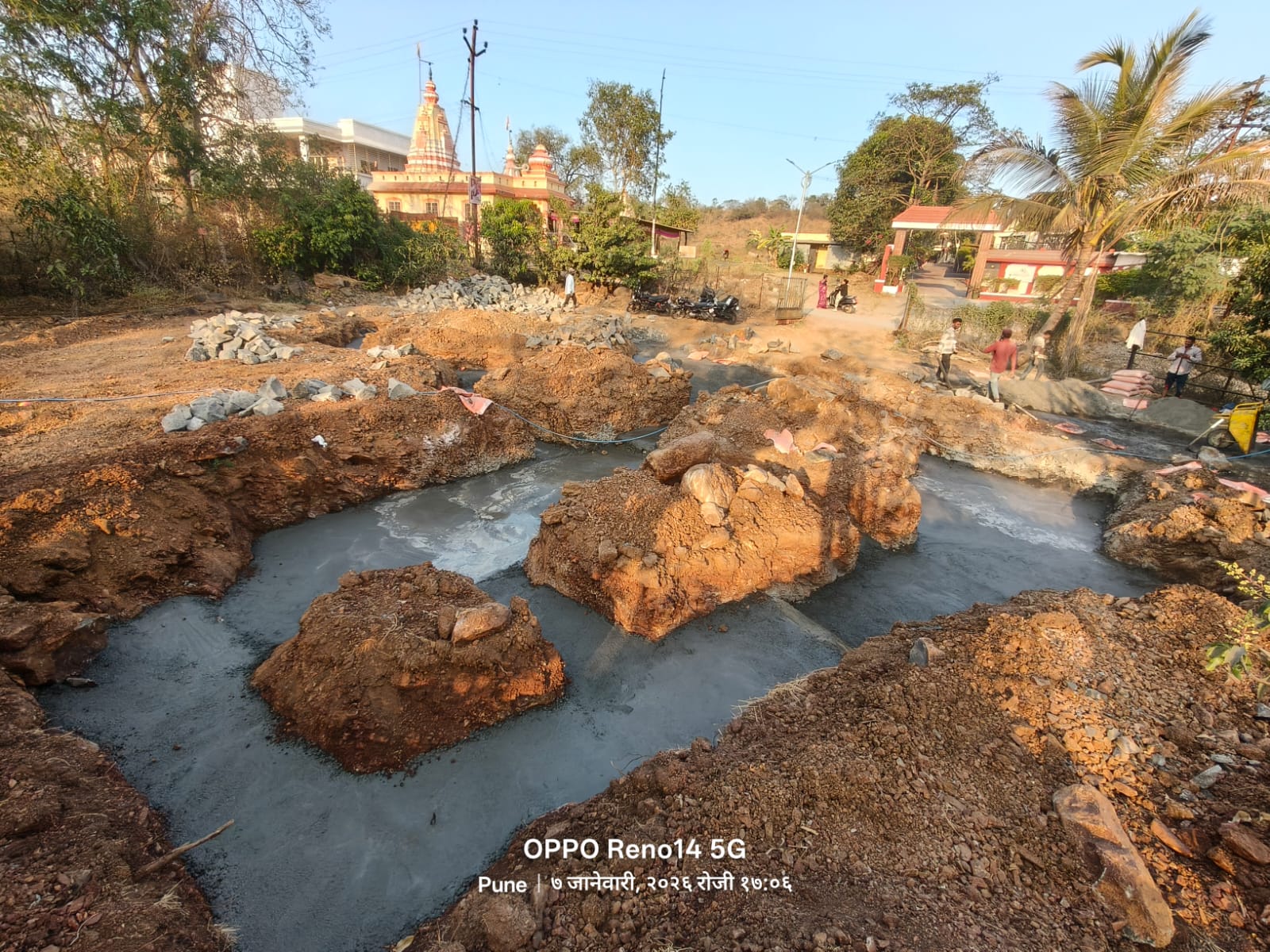PCC layer poured across the foundation trenches, with excavated boulders and stones stored aside in the background